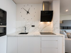 A modern kitchen with a built-in clock, a stainless steel range hood, and a marble backsplash. - Beachfront 2BR Apartment in Central Malaga with Terrace and Modern Amenities (Málaga)