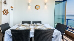 A dining area with a table set for six, surrounded by wicker chairs, on a wooden deck with a view of the sea. - Seafront penthouse with WiFi, parking, and air conditioning in Malaga (Málaga)
