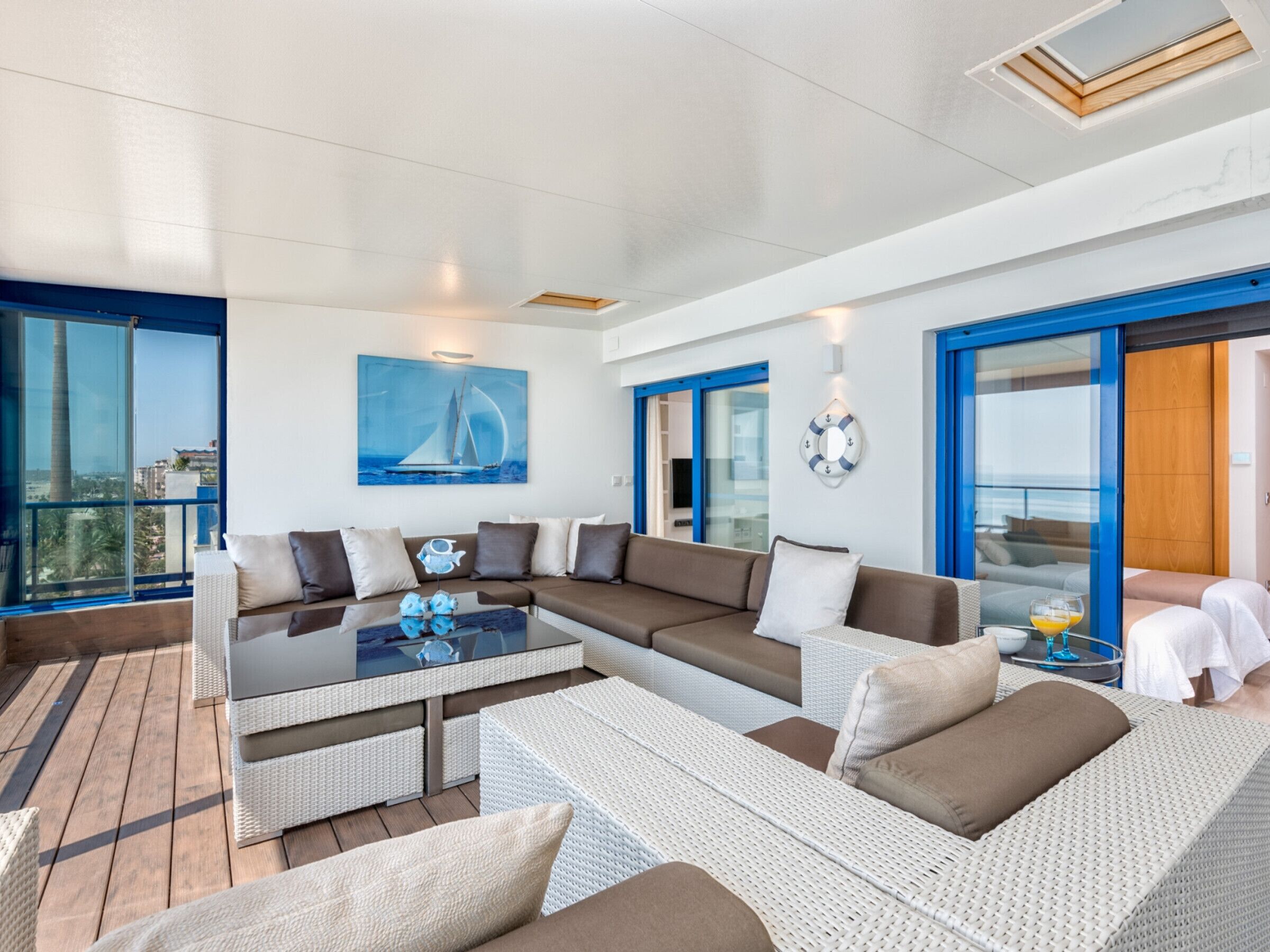 Un salon moderne doté d’un grand canapé d’angle, d’une table basse en verre et offrant une vue sur la mer grâce à de grandes fenêtres.