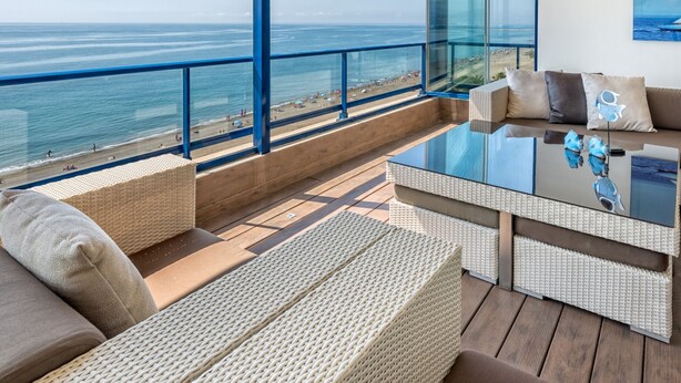 A modern balcony with wicker furniture, a glass table, and a view of the beach and ocean. - Seafront penthouse with WiFi, parking, and air conditioning in Malaga (Málaga)