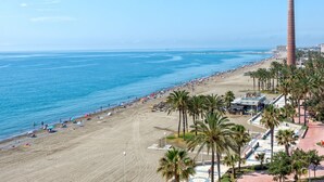 A beach with a tall chimney, palm trees, and a clear blue sky. - Seafront penthouse with WiFi, parking, and air conditioning in Malaga (Málaga)