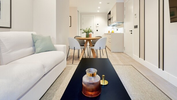 Ein modernes Wohnzimmer mit einem weißen Sofa, einem Esstisch mit Stühlen und einer Küche im Hintergrund.