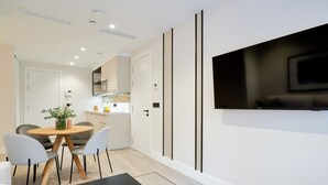 Ein modernes Wohnzimmer mit einem schwarzen Couchtisch, einem an der Wand montierten Fernseher und einem Essbereich mit einem Holztisch und Stühlen.