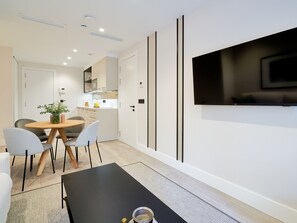 Ein modernes Wohnzimmer mit einem schwarzen Couchtisch, einem an der Wand montierten Fernseher und einem Essbereich mit einem Holztisch und Stühlen.
