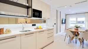 Eine moderne Küche mit einer zentralen Kochinsel, einem Essbereich mit rundem Tisch und einem an der Wand montierten Fernseher.