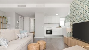 A modern living room with a sofa, two woven ottomans, a TV, and a wooden side table. - Chic 3-bedroom apartment with terrace, Wifi, and parking in Malaga (Málaga)