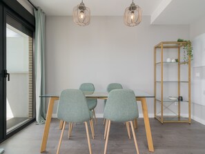 Un comedor moderno con una mesa de vidrio, cuatro sillas color turquesa y dos lámparas colgantes.