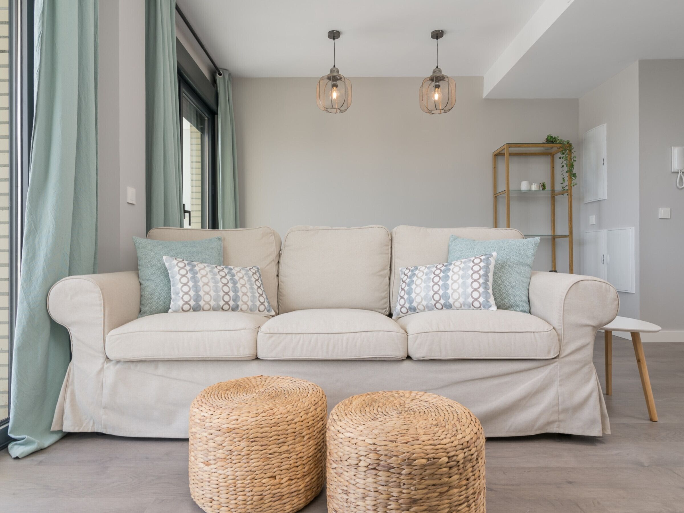 A living room with a beige sofa, two woven ottomans, and a wooden side table.