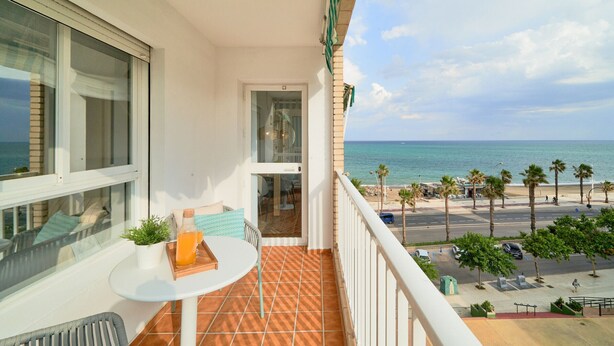 Een balkon met uitzicht op het strand, een tafel met een fles en glazen, en een stoel.
