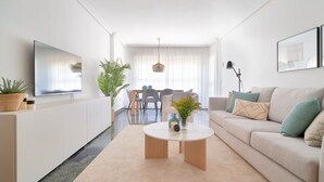 Een moderne woonkamer met een bank, een salontafel, een televisie en een eethoek met stoelen en een tafel.