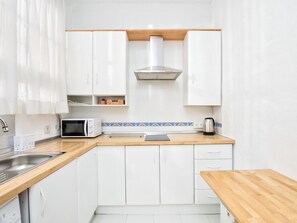 Une cuisine compacte avec des meubles blancs, un four à micro-ondes, une bouilloire et un plan de travail en bois.