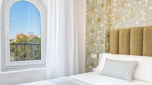 Een hotelkamer met een groot bed, uitzicht op gebouwen door een raam en een behang met een bloemenpatroon.