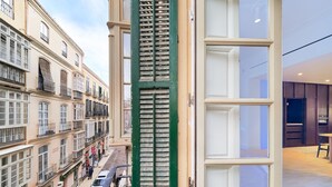 Blick vom Balkon auf eine Straße mit Gebäuden, einer grünen Rolltür und einem modernen Innenraum mit Essbereich.
