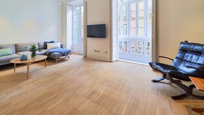 Ein geräumiges Wohnzimmer mit einer Couch, einem Couchtisch, einem Ledersessel und einem an der Wand montierten Fernseher.