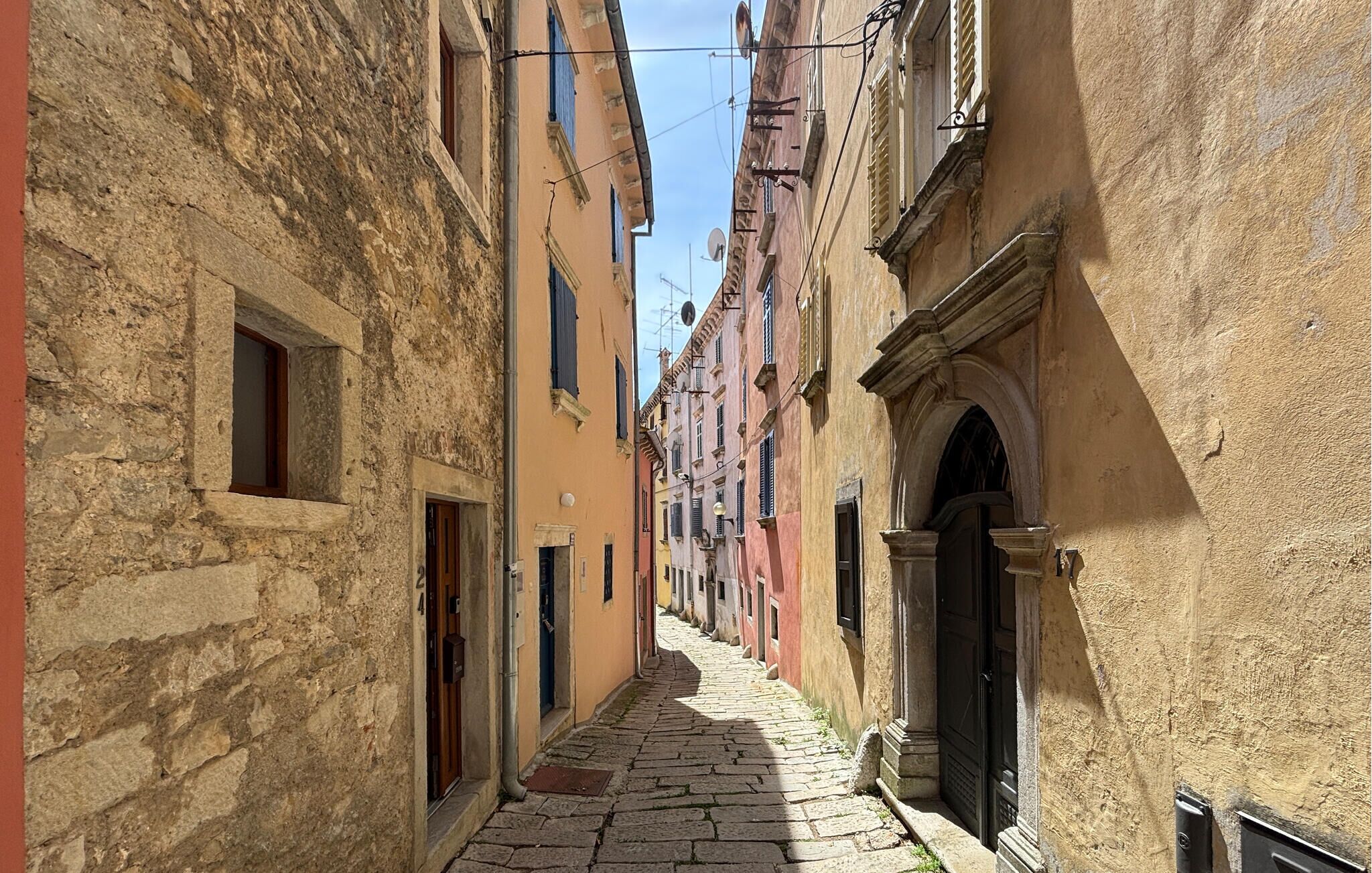 A narrow cobblestone street flanked by historic buildings with arched doorways and traditional shutters.