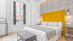 Ein modernes Schlafzimmer mit einem großen Bett, einem Nachttisch, einer Bank und einer Wand mit Muster.