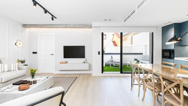 A modern living room with a flat-screen TV, a dining area with wooden chairs, and a view of a garden through glass doors. - Central Málaga: Modern 2BR Apartment with Patio, Terrace, and Free Parking (Málaga)