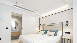 A modern bedroom with a large bed, bedside tables, a mirror, and a bathroom with a sink and vanity. - Central Málaga: Modern 2BR Apartment with Patio, Terrace, and Free Parking (Málaga)