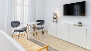 Una habitación moderna y minimalista con una cama, una pequeña mesa de comedor con sillas, un televisor montado en la pared y un mueble con un adorno encima.