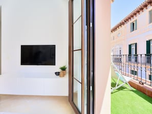 Una sala de estar moderna con un televisor de pantalla plana montado en la pared, una pequeña planta en maceta y un mueble blanco.