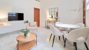 A modern living room with a flat-screen TV, a round wooden coffee table, a sofa, and a dining table with chairs. - Elegant 2-Bedroom Apartment in Central Málaga, Close to Key Attractions (Málaga)