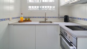 A kitchen with white tiled walls, a window with decorative bars, a sink, a coffee maker, and an oven. - Elegant 2-Bedroom Apartment in Central Málaga, Close to Key Attractions (Málaga)