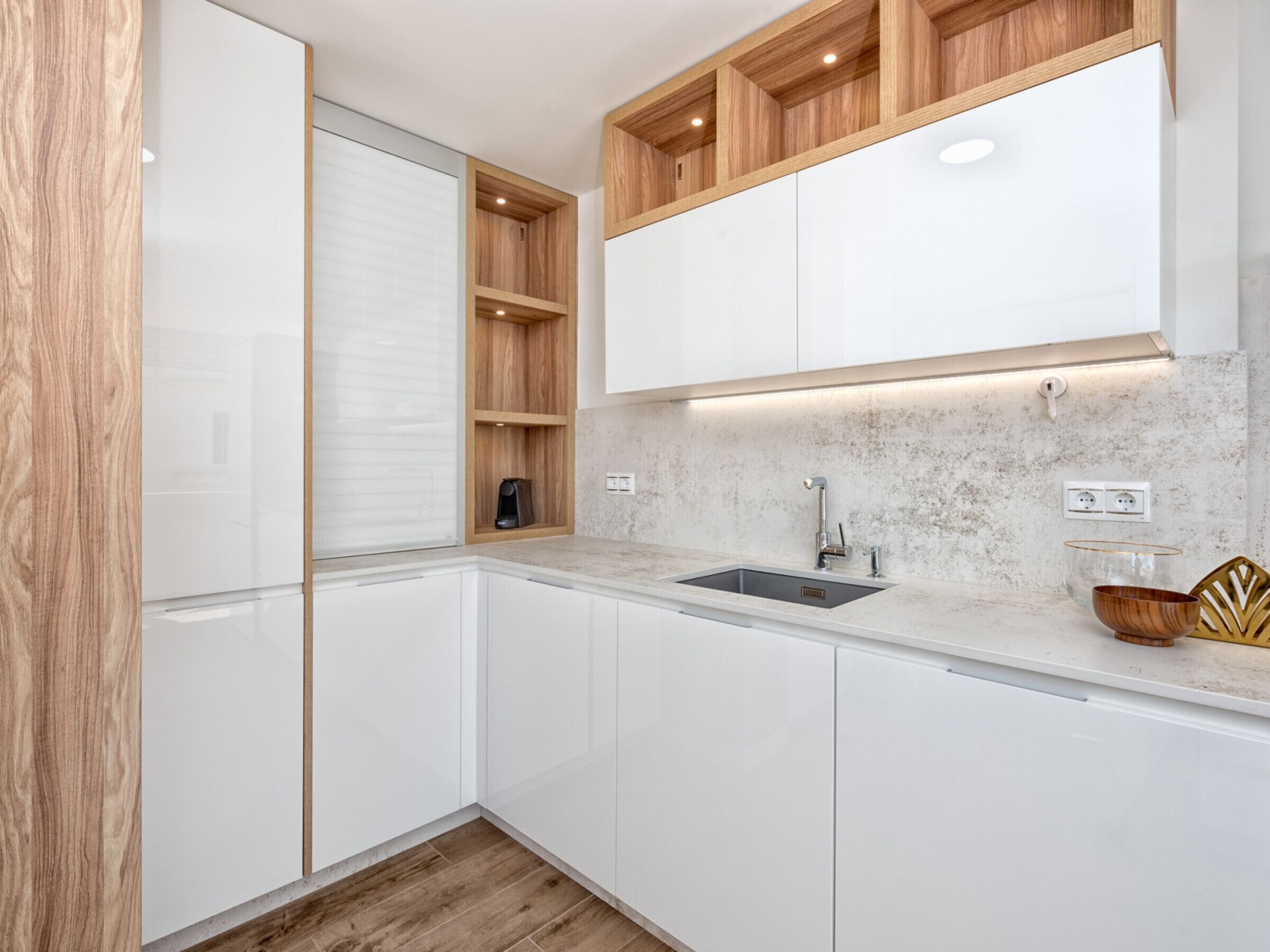 Una cocina moderna con armarios blancos, encimera de mármol y estanterías de madera.