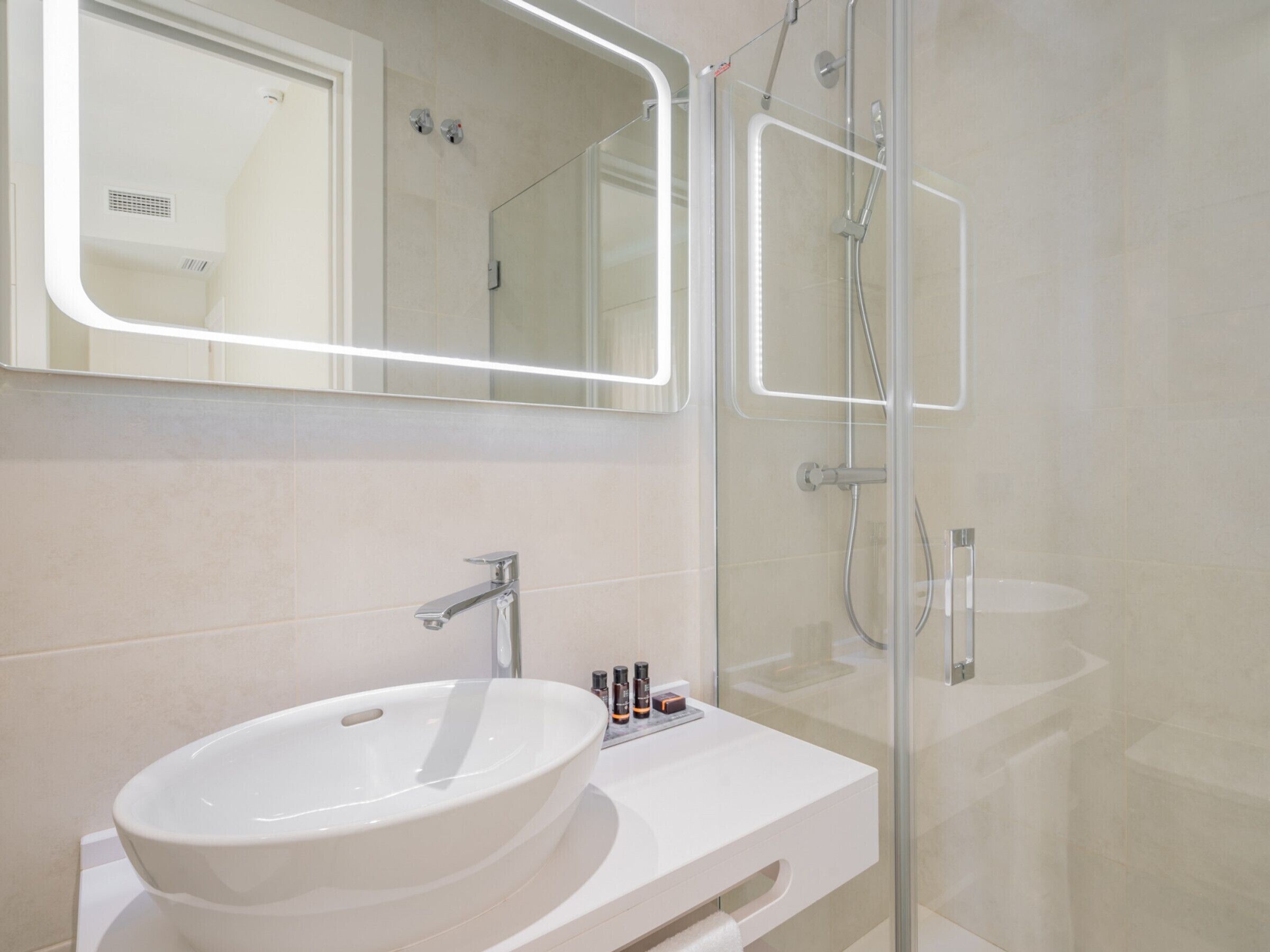 A modern bathroom with a large white sink, a mirror, and a glass-enclosed shower area.