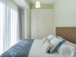 Ein ordentlich bezogenes Bett mit einer blau-weißen Tagesdecke, weißen Kissen und einem braunen Kopfteil.