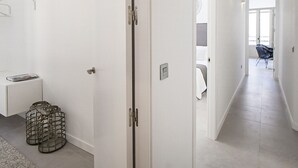 Un corridoio moderno di un hotel con pareti bianche, una porta, una piccola scrivania con una rivista e una sedia sullo sfondo.