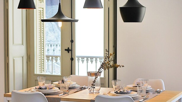 Un tavolo da pranzo apparecchiato con piatti, bicchieri e posate, illuminato da tre lampade a sospensione.