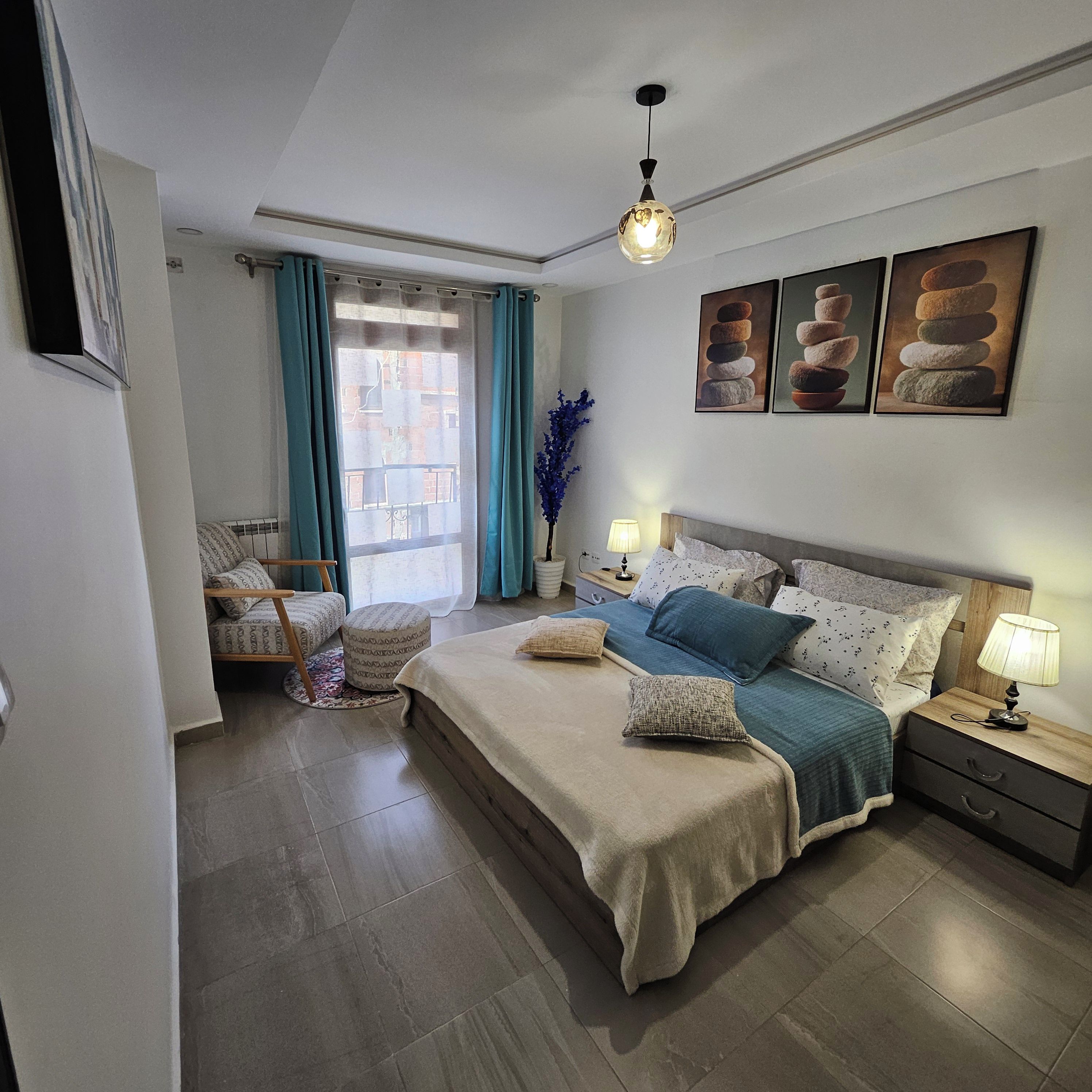 Ein Schlafzimmer mit einem großen Bett, Nachttischen, einem Fenster mit Vorhängen und Wandbildern.