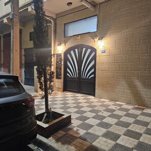 A building entrance with a checkered pavement, a black gate with a fan-like design, and a street lamp.