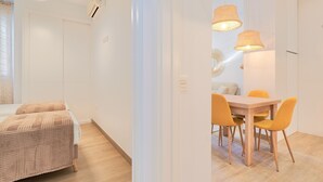 Een moderne, goed verlichte kamer met een bed, een eettafel met stoelen en een plafondlamp.