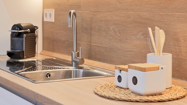 Een moderne keuken met een roestvrijstalen spoelbak, een koffieapparaat en houten kruidenpotjes op een geweven placemat.