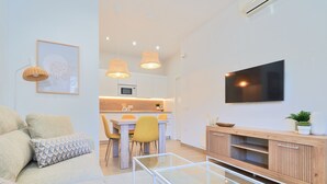 Een moderne woonkamer met een bank, een glazen salontafel en een aan de muur bevestigde televisie.