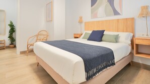 Een moderne slaapkamer met een groot bed, een houten hoofdbord, een nachtkastje, een stoel, een lamp en een kunstwerk aan de muur.
