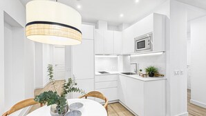 A modern kitchen with white cabinetry, a microwave, and a dining area with a round table and chairs. - Charming Apartment Near Alcazaba Málaga with Modern Amenities, WiFi, and A/C (Málaga)