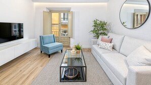 A modern living room with a flat-screen TV, a blue armchair, a glass coffee table, a grey sofa, and a large mirror. - Charming Apartment Near Alcazaba Málaga with Modern Amenities, WiFi, and A/C (Málaga)