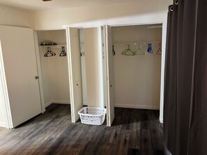 Une pièce avec un plancher en bois, une armoire blanche avec des cintres et un panier blanc.