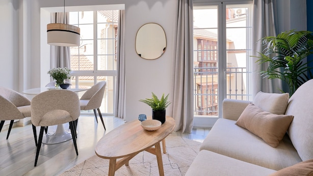 Una sala de estar moderna con un sofá, sillas, una mesa de comedor y un ventanal con cortinas.