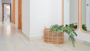 Un pasillo con una cesta de mimbre que contiene plantas verdes, un espejo grande y una puerta con marco de madera.