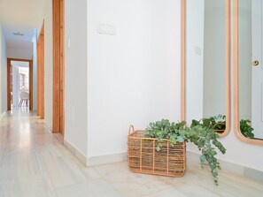 Un pasillo con una cesta de mimbre que contiene plantas verdes, un espejo grande y una puerta con marco de madera.