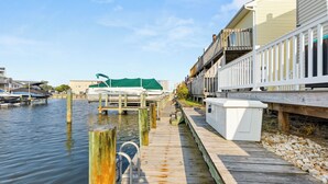 Une jetée en bois avec des bateaux, un bâtiment blanc doté d’un balcon et un ciel dégagé.