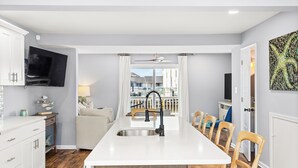 Une cuisine moderne dotée d’un îlot central, de meubles blancs et d’un téléviseur à écran plat fixé au-dessus de l’îlot.