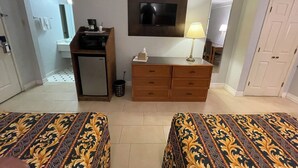 Una habitación de hotel con dos camas, un escritorio pequeño con cafetera, televisor, lámpara y espejo.