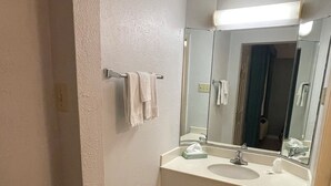 Un baño con lavamanos, espejo, toallero y un cubo de basura.