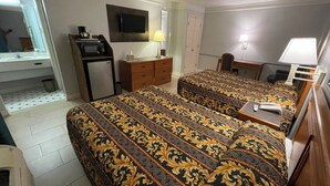 Habitación de hotel con dos camas, un escritorio, una silla, un televisor, un refrigerador pequeño y un baño.
