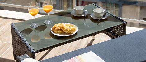 A balcony with a glass table set with croissants, two glasses of orange juice, and a cup and saucer.