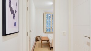 A hallway with a framed abstract artwork, a wooden bench, and a window with a stained glass design. - Charming 2-Bedroom Apartment in Central Malaga with Modern Amenities (Málaga)
